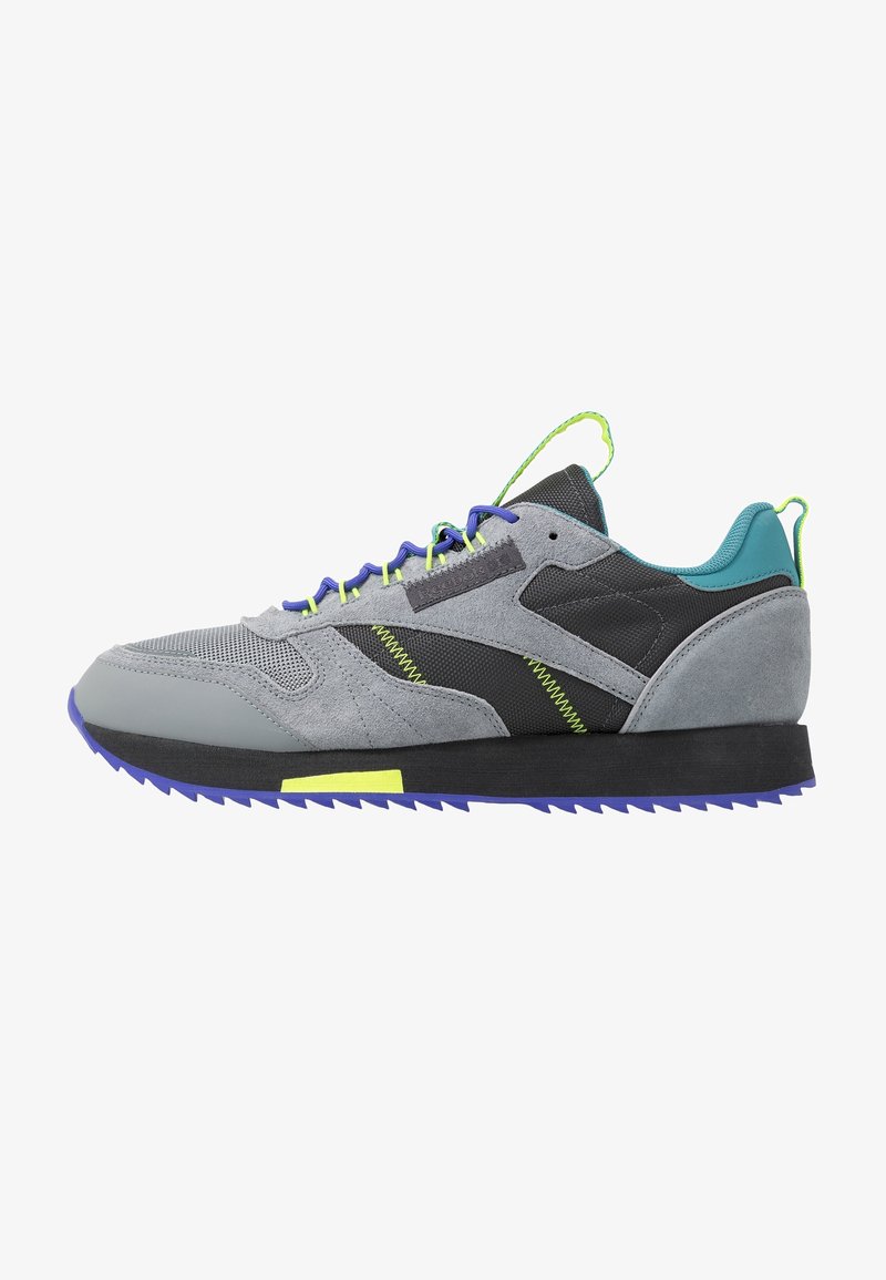 Scarpa da ginnastica grigia con una combinazione di parte superiore in suede e mesh, accenti blu, lacci verde neon e suola nera testurizzata con bordo viola.