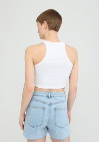 Weißes, kurzes Tanktop mit geripptem Textur und breiten Schulterträgern, kombiniert mit hellblauen Denim-Shorts mit ausgefransten Säumen.