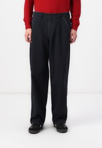 Navy blue trousers in a relaxed fit, featuring front pockets and subtle stitching details. Paired with black sneakers.