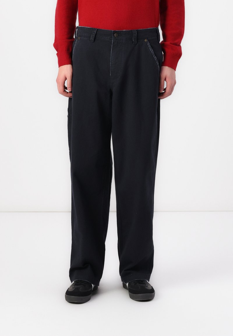 Navy blue trousers in a relaxed fit, featuring front pockets and subtle stitching details. Paired with black sneakers.