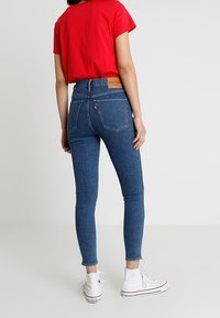 Úzké džíny v tmavě modré barvě s vysokým pasem a zadními kapsami. Kombinovány s červeným tričkem a bílými vysokými teniskami.