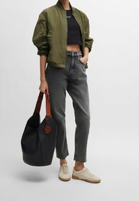 Oliivivihreä pommikurttupaita, musta crop-top, harmaat farkut, vaaleanbeige tennarit sekä musta käsilaukku, jossa on ruskeita yksityiskohtia ja logokuvio.