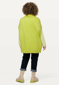Maglione oversize verde lime con texture a coste, maniche a strisce crema, jeans scuri e stivali beige con suole verde lime.