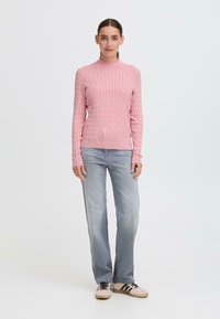 Maglione rosa a coste con un collo alto, abbinato a jeans dritti grigio chiaro e sneakers beige con strisce nere.