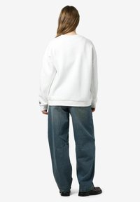 Witte oversized sweater met een ronde hals, gecombineerd met een losvallende, licht versleten blauwe spijkerbroek. Effen kleur, casual ontwerp.