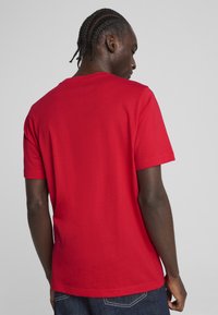 Rotes T-Shirt mit kurzen Ärmeln aus Baumwolle, mit Rundhalsausschnitt und einfachem Rücken, kombiniert mit dunklen Jeans.