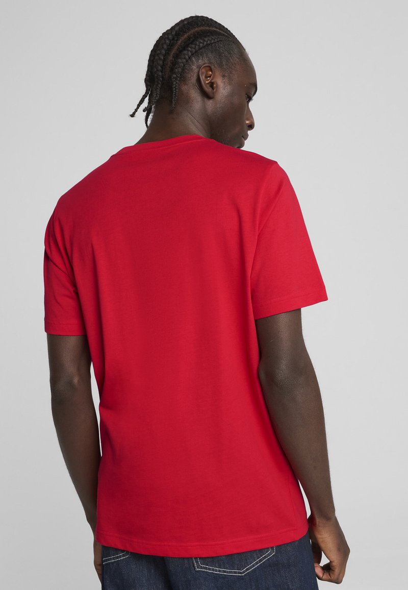 T-shirt rouge à manches courtes en coton, avec un col rond et un dos uni, associé à un jean en denim foncé.