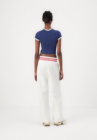 Marinblå kort topp med vit kant som är parat med grå sweatpants med röd och vit randig midja. Mjuk tyg, lös passform, minimal mönster.