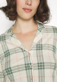 Kariertes Schlafanzugoberteil in Grün, Pink und Cremefarben. Verfügt über einen weichen Stoff, Knopfleiste und kontrastierende Paspelierung entlang des Kragens und der Knopfleiste.