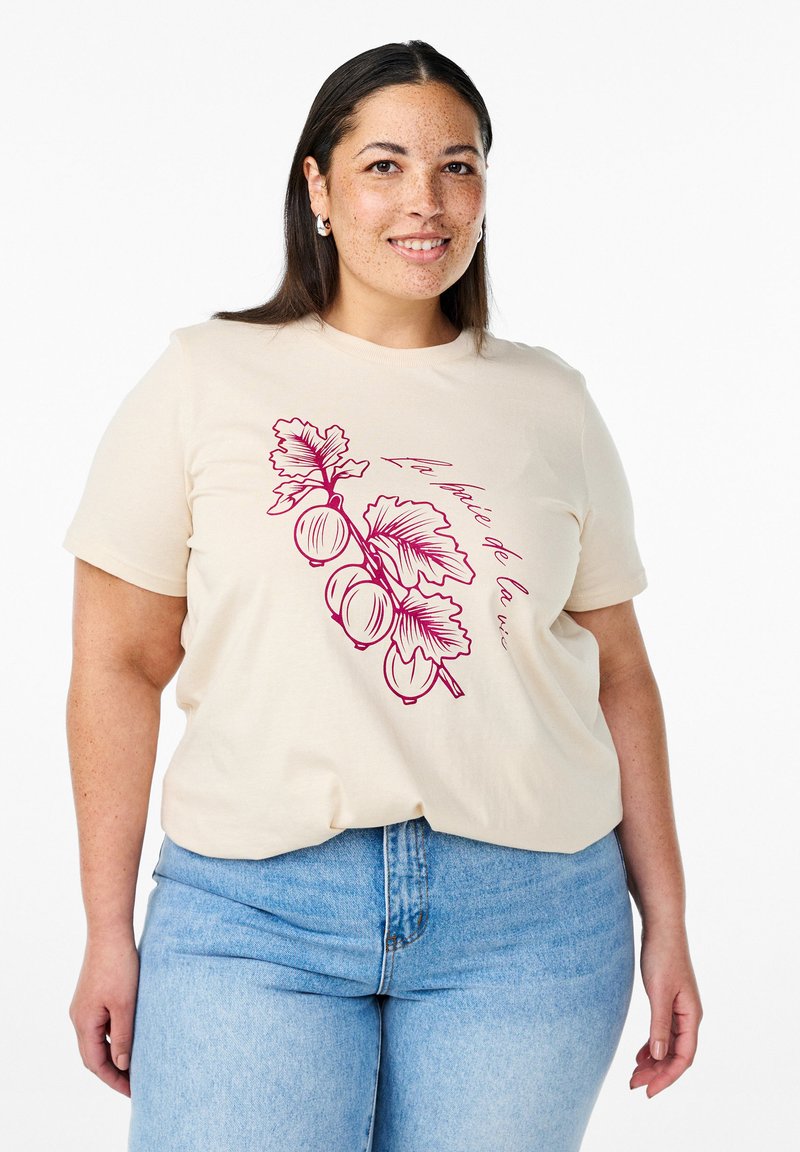 Beige cotton t-shirt featuring a red botanical graphic of leaves and fruit. Classic crew neck, short sleeves, relaxed fit. Denim jeans visible.