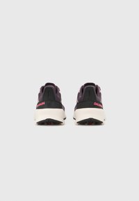 Ζευγάρι μωβ και μαύρα αθλητικά παπούτσια Salomon με παχιά λευκή σόλα, από πίσω, πάνω σε απλό φωτεινό φόντο.