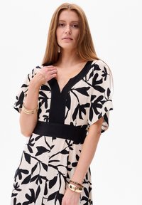 Zwart-wit bloemenpatroon jurk met een diepe V-hals, korte mouwen en een zwarte tailleband. Glad materiaal met een ontspannen pasvorm.