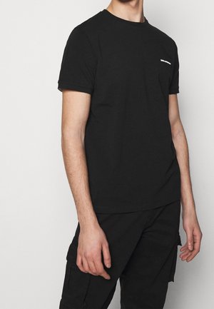 T-shirt en coton noir à manches courtes, col rond et avec un petit logo blanc sur la poitrine gauche. Texture lisse et coupe régulière.