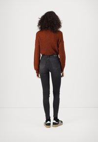 Suéter de punto color óxido, jeans ajustados negros y zapatillas negras con acentos blancos. La vista trasera muestra el diseño ajustado y el suéter texturizado.