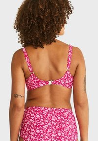 Rosa blommig bikiniöverdel med justerbara band och ett spänne på ryggen. Har ett livligt mönster med små vita blommor och en slät textur.