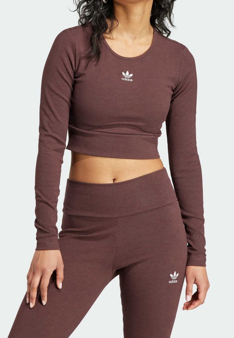 Brun ribbad crop top med lång ärm, med rund halsringning och vit Adidas-logga. Kombinerad med matchande högmidjade leggings.