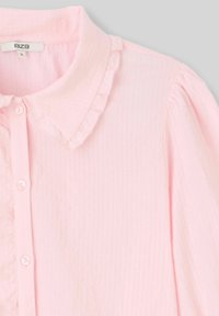 Blouse rose clair, texturée, avec un col à volants, fermeture à boutons à l'avant et manches froncées. Fabriquée en tissu doux et léger.