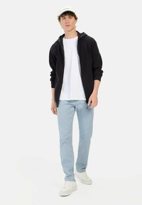 Czarna bluza z kapturem, biała koszulka, jasnoniebieskie spodnie i białe sneakersy. Bluza ma kaptur i boczne kieszenie. Miękka faktura materiału.