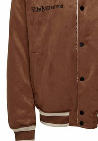 Veste bomber en faux daim brun avec des boutons-pression noirs, poche latérale et poignets côtelés avec des rayures blanches et brunes. Détail du logo brodé.