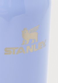 Μπλε επιφάνεια με ασημένιο λογότυπο Stanley που απεικονίζει μια βαριά φτερωτή με κορώνα πάνω από το όνομα της μάρκας.