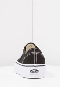 Svart kanvas slip-on sko med vit söm och sidstripe, med en vit gummisula och "Vans Off The Wall" logotyp på hälen.
