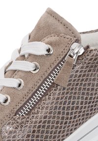 Close-up of beige suede sneaker with white laces, metal eyelets, side zipper, and glittery patterned fabric near sole.