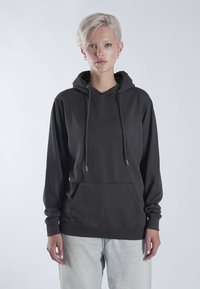 Sweatshirt à capuche noir en tissu doux, avec une poche kangourou, des accents de cordon de serrage et des poignets et un ourlet côtelés. Modèle portant un jean clair.
