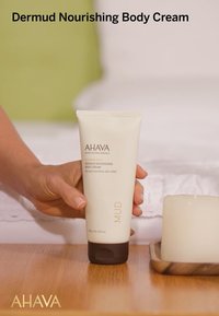 Krem do ciała Dermud Nourishing w miękkiej beżowej tubie z brązową nakrętką, oznakowany szczegółami produktu oraz wyraźnym logo, wyeksponowany na drewnianej powierzchni.