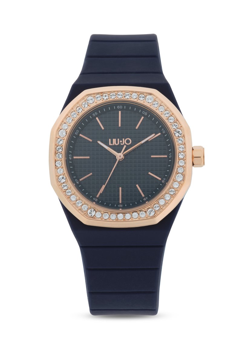 Orologio con cinturino in silicone blu navy e lunetta ottagonale in oro rosa. Accenti di cristallo circondano un quadrante scuro texturizzato con lancette e indicatori delle ore in oro rosa.