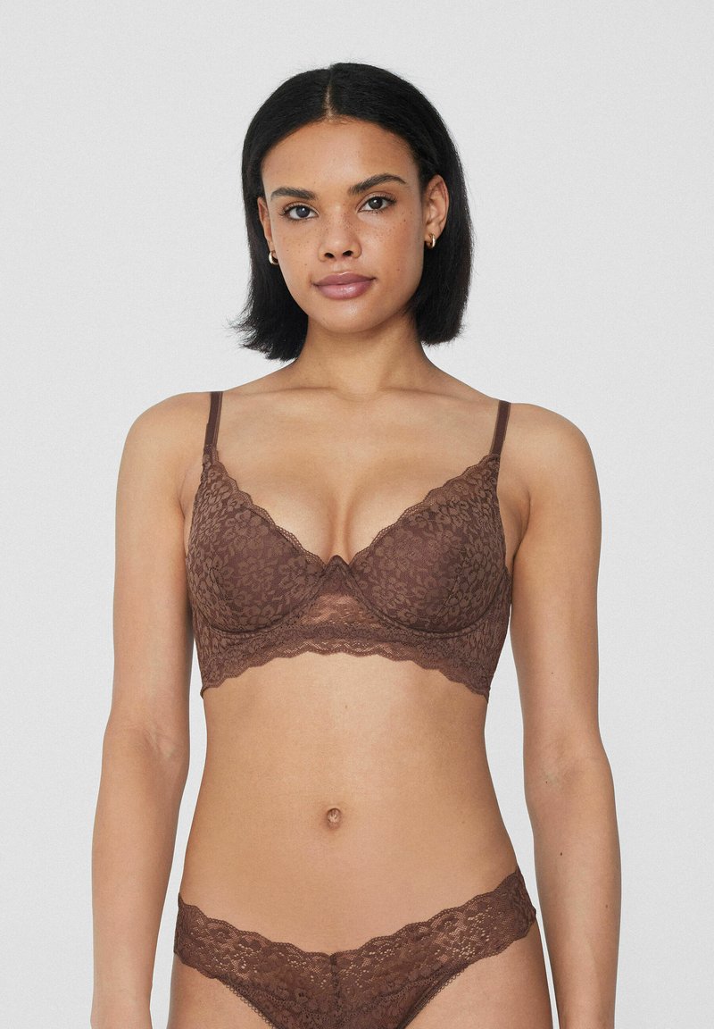 Sujetador de encaje marrón con aro y bordes festoneados. Tanga de encaje a juego con un patrón floral. Textura suave, tirantes ajustables.