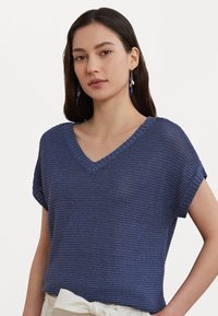 Top de punto azul marino con un escote en V pronunciado, mangas cortas y un acabado texturizado. Presenta un ajuste relajado y una tela ligera y transpirable.