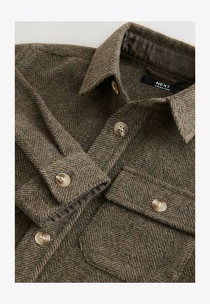 Barna halszálkás ingdzseki texturált anyagból. Két zsebével, gombos elülső résszel és hegyes gallérral rendelkezik.