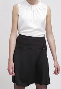 Valkoinen hihaton pusero, jossa on laskostettu pääntie, yhdistetty mustaan A-linjaisiin hameeseen, jossa on leveä vyötärö ja suorakulmainen solkoyksityiskohta.