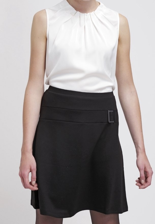 Valkoinen hihaton pusero, jossa on laskostettu pääntie, yhdistetty mustaan A-linjaisiin hameeseen, jossa on leveä vyötärö ja suorakulmainen solkoyksityiskohta.