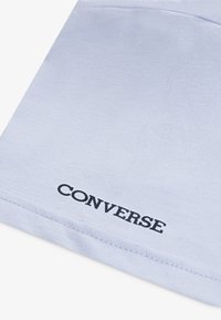 Vaaleansininen puuvillapaita, jossa on ribbed-rakenne, ja jonka vasemmassa alakulmassa on tummansinisellä painettu "CONVERSE"-logo.