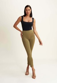Top aderente nero e leggings verdi oliva realizzati in tessuto elasticizzato. I leggings presentano un'alta vita e un design senza cuciture. Tacchi trasparenti.