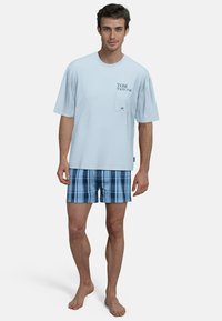 Light blue cotton t-shirt with front pocket and brand logo, paired with plaid drawstring shorts in various shades of blue.