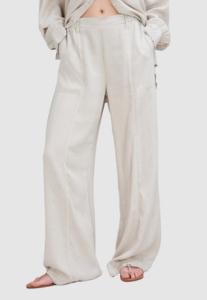 Pantalons larges beige clair en tissu doux, avec des poches latérales, une taille élastique et de subtils détails de couture.