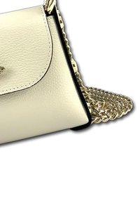 Crème lederen handtas met zwarte afwerking; beschikt over een gouden schouderband en een klep met een decoratieve sluiting. Oppervlakte met textuur zichtbaar.