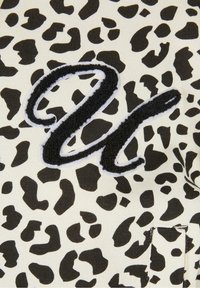 Tissu imprimé léopard noir et blanc avec une grande lettre cursive noire texturée "u" cousue dessus.