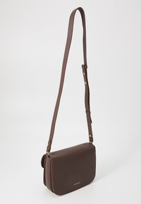 Brown faux leather shoulder bag with a textured finish, flat shape, adjustable strap, and gold-tone hardware accents. Closure on the top.