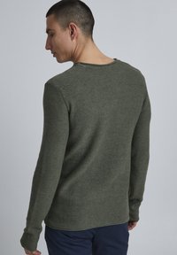 Grüner Strickpullover mit langen Ärmeln und Rundhalsausschnitt, aus strukturiertem Stoff mit geradem Saum. Rückansicht, die die Details von Schulter und Ärmeln zeigt.