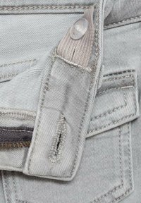 Sivi jeans material z vidnim zadrgo, zapiranjem na gumb in šitimi detajli. Ima žep z raztrganimi robovi in teksturirano površino.