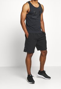 Czarny sportowy tank top z logo, do tego czarne szorty z bocznymi rozcięciami. Czarne buty sportowe. Teksturowana tkanina, sportowy design.