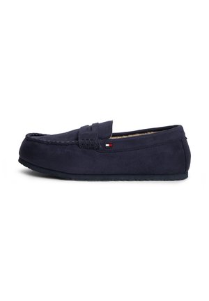 Chausson mocassin en daim bleu marine avec des détails cousus, une doublure intérieure douce, une semelle plate et un petit logo rectangulaire de la marque sur le côté.