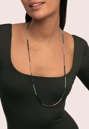 Collar largo de cuentas con cuentas azules, verdes, rosas y marrones con acentos dorados, colgando elegantemente sobre una blusa verde oscuro.