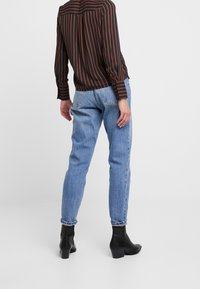 Camiseta de manga larga a rayas negras y naranjas combinada con pantalones vaqueros de mezclilla azul claros y botas negras hasta el tobillo. Los pantalones están doblados en los tobillos.