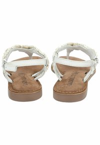 Sandales blanches à semelle beige douce, avec un design de sangle texturée et des accents décoratifs le long des bords. Sangle de cheville réglable incluse.