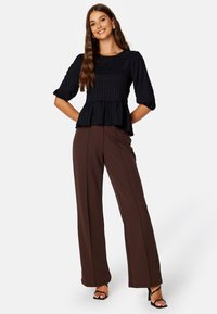 Zwarte gestructureerde peplumtop met 3/4 mouwen, gecombineerd met bruine wijde broekspijpen. Het geheel heeft een getailleerde pasvorm en een fijne stof.