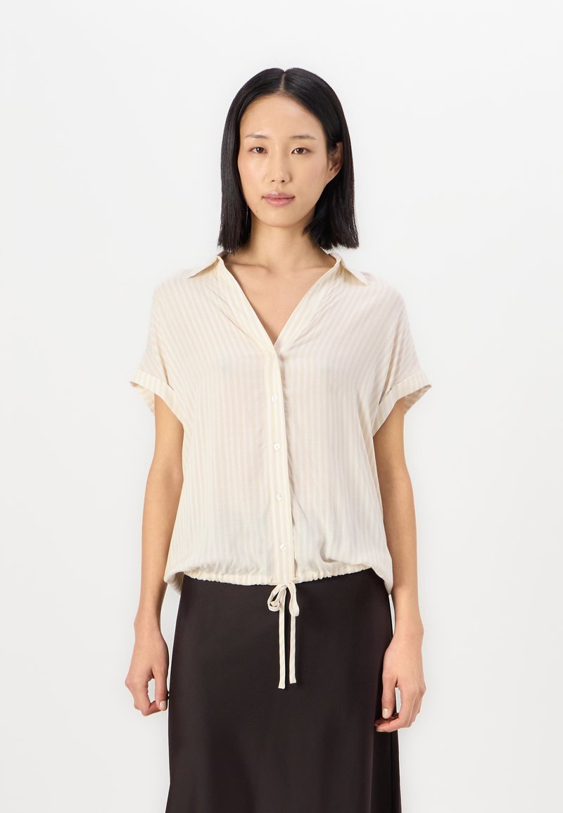 Light beige short-sleeve blouse with vertical stripes, a collar, and a drawstring hem. White buttons down the front add detail.